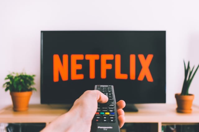 hand holding remote pointed at tv with netflix logo