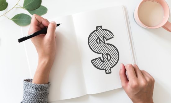 open journal with hands drawing a money sign
