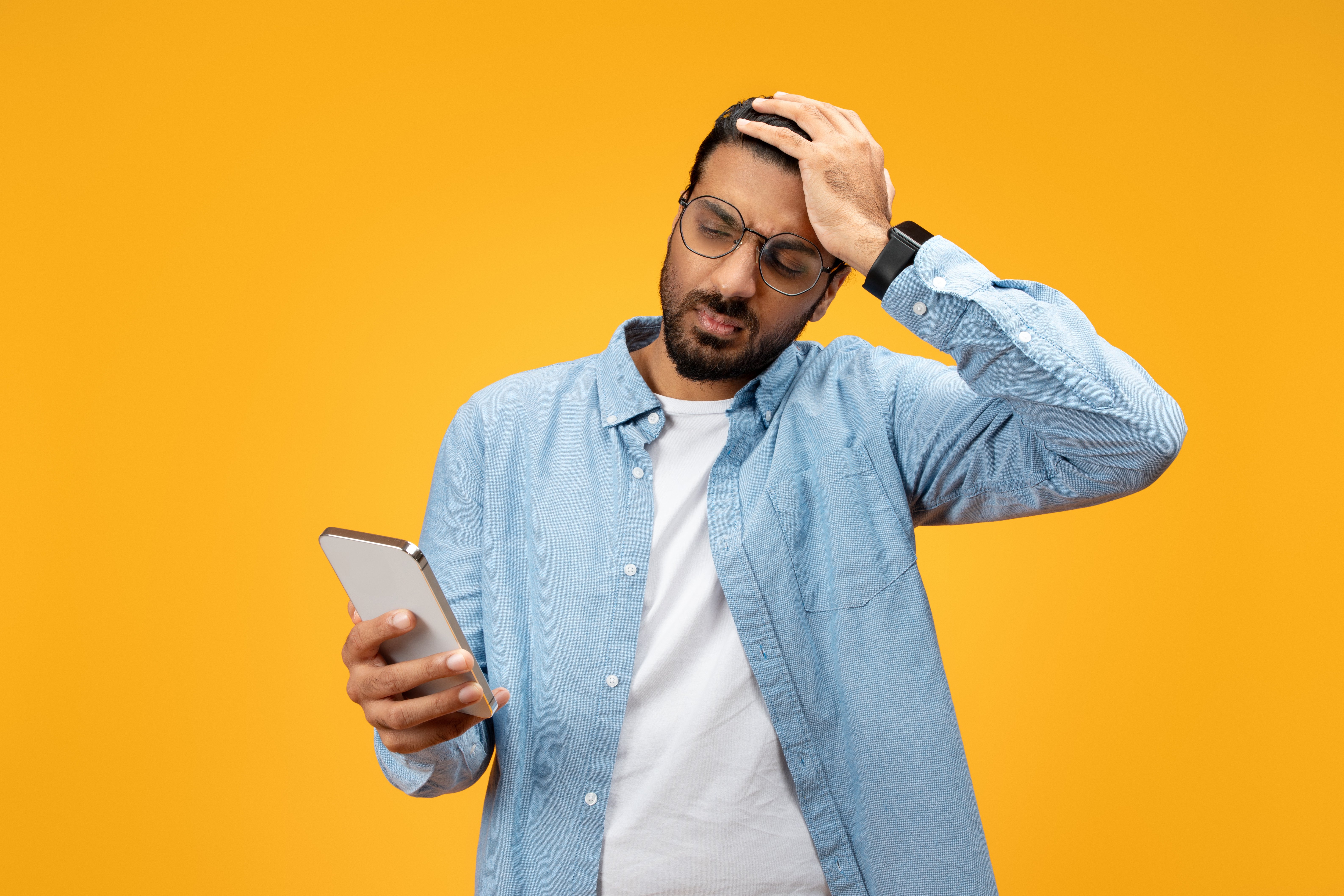 a-perplexed-man-in-a-blue-shirt-holds-his-smartpho-2024-01-04-21-23-25-utc