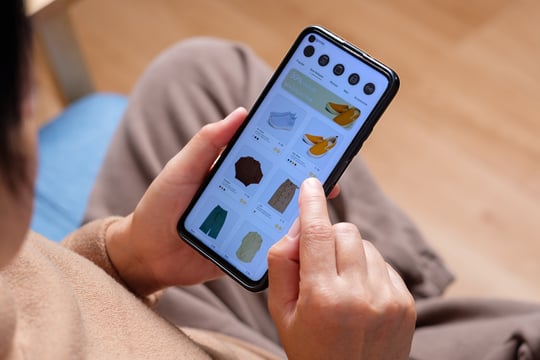 Background image of close up hand browsing shopping fashion mobile app on sofa at home