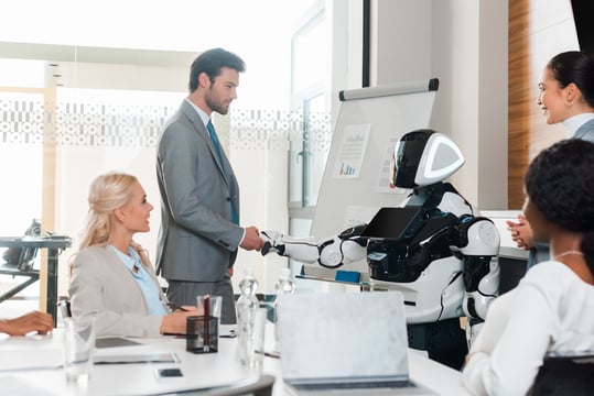 Background image of handsome businessman shaking hands with robot near multicultural colleagues sitting in conference