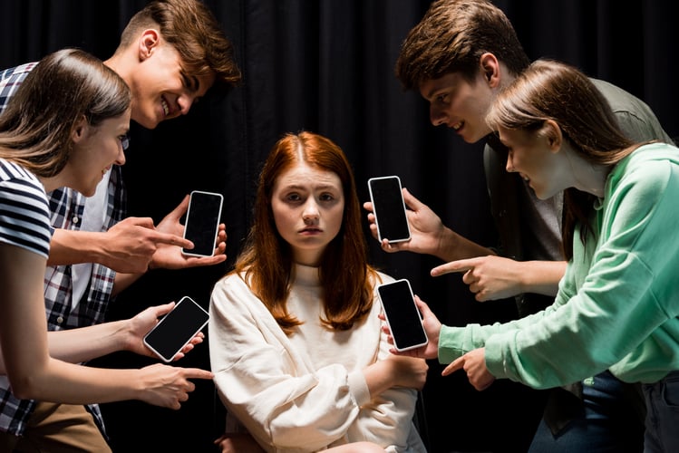 Background image of smiling teenagers pointing with fingers at girl during bullying and holding smartphones with blank