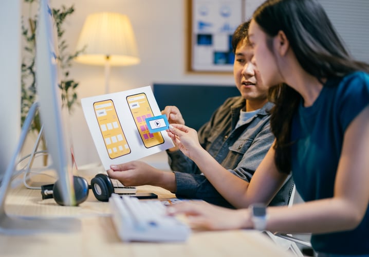 Background images Two asian ui/ux designers are discussing a mobile app wireframe prototype at their desks in the offi