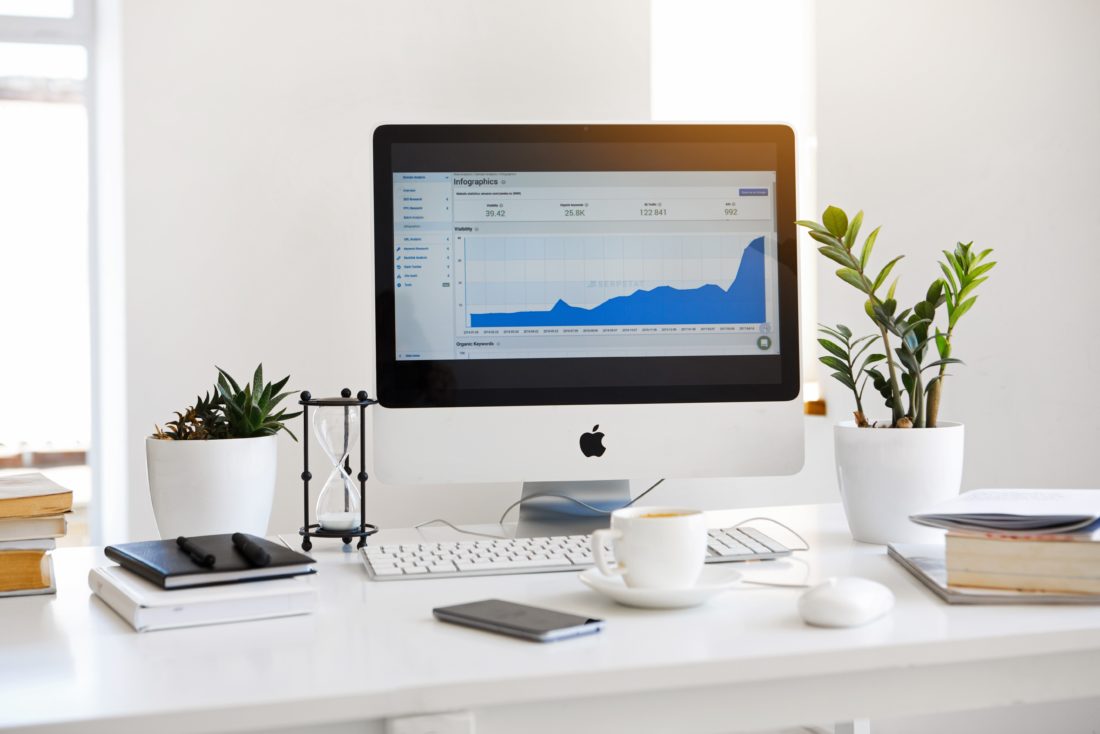 Office desk with multiple accessories and an apple display monitor showcasing some mobile app marketing analytics